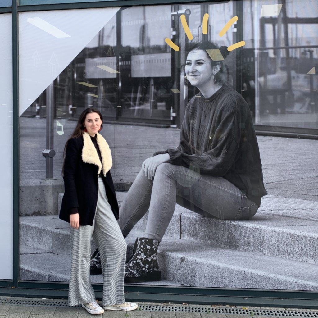 Hebe at the university standing under a giant photograph of herself